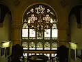 First floor landing view of stained-glass window with chandelier above staircase. View at max resolution to see Madonna and Child in top roundel.