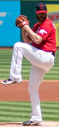 A baseball player in a red jersey and white pants in his wind-up preparing to pitch a ball from the mound