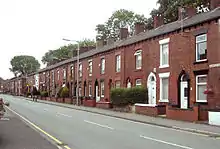 View down a street of two-storey brick-built terraced houses.