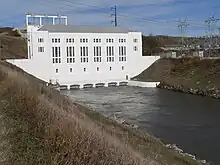 Powerhouse with tailrace canal running out of base; electrical transformers on canal bank at right