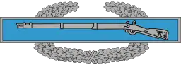 A metal device depicting a blue bar with a rifle, in front of a wreath of silver leaves.