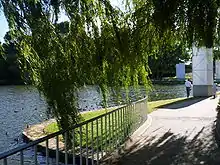 An inlet of the lake, landscaped with concrete footpaths, safety rails and shady trees. Many ducks are swimming next to shore.