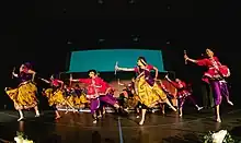 Collegiate Garba-Raas team on stage, captured during Raas section of performance (holding dandiyas) dressed in traditional attire