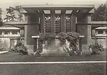  Low building with ivy draped terrace and three prominent vertical windows with tall trees in the background