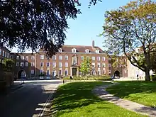 three and four storey Georgian-style red brick building with eleven central bays and two wings, with trees and lawns in the foreground