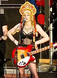 Woman with hands on hips, with a guitar, speaking into a microphone