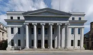 A three-story light-colored stone building. In the front a pedimented central pavilion with six Ionic columns projects. Between the second and third stories of the main facade there is a large molded cornice.