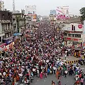 A dense crowd of several hundred people on a street lined with shops and ads