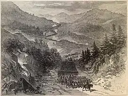 A lithograph in black and white of a road winding through a mountainous region. An army of thousands is marching along the road, led by a military officer on a horse.