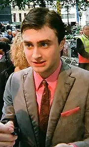 A young male is signing his signature with a fan. His hair is slicked over to the side.