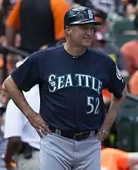 A man in a blue baseball jersey with "Seattle" on the chest in white standing with his hands on his hips