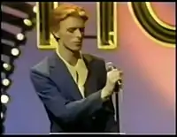 A red-haired man in a suit standing next to a microphone