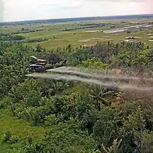 A UH-1D helicopter from the 336th Aviation Company sprays a defoliation agent over farmland in the Mekong Delta.