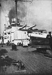 Two large gun turrets on a warship. Thick black smoke billows from the funnels.