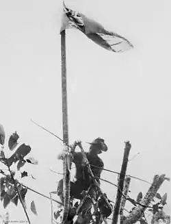 A soldier wearing a turned-up slouch hat raises the Australian flag