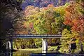 Red, green and orange fall foliage surrounds a small bridge spanning a quiet, rocky Lee Creek