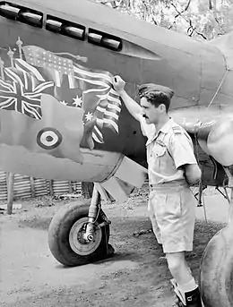 Mustachioed man in forage cap and khaki uniform, next to a single-engined military aircraft