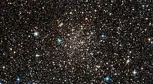 A loose scattering of small dull white dots on a black background with a few brighter coloured stars