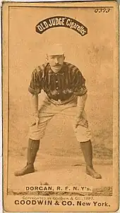 A baseball player standing facing the camera with his hands resting on his knees