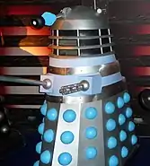 An original Dalek, coloured mostly silver and grey, with blue balls protruding from the skirt.