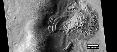 Layered feature that is probably the remains of a once widespread unit that fell from the sky, as seen by HiRISE under the HiWish program.   Dipping layers are common in some regions of Mars.  They may be the remains of mantle layers. Another idea for their origin was presented at 55th LPSC (2024) by an international team of researchers.  They suggest that the layers are from past ice sheets.