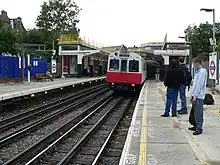 Red-and-white train pulling into outdoor station, with passengers waiting on platform