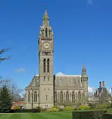 A tall clock tower in shape rather like Big Ben at Westminster; behind this is a Gothic chapel with an apse on the left and a turret on the right