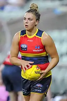 A female athlete in a sleeveless guernsey holding a football