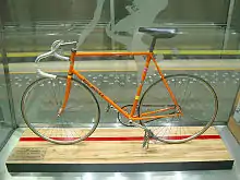 An orange bicycle behind glass.