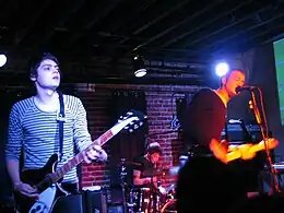 Several men performing onstage, playing instruments and singing into a microphone