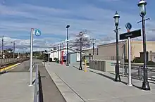 A train platform with concrete pavement, street lamps, signage, and a ramp for wheelchair access