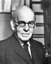 Photograph of a bald man wearing a suit and glasses