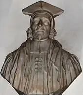 A stone bust of a man (head and shoulders), with beard, cap and robes