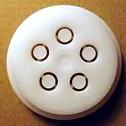 White plastic disk with five ring-shaped holes in it