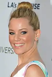 Elizabeth Banks, a blonde-haired caucasian woman in her early 40s, wears a white dress. She wears her blonde hair up in a ponytail.