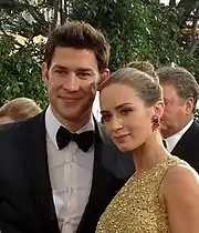 A man and a woman stand next to each other as they smile for a camera