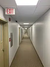 A white hallway lit by fluorescent lighting with an exit sign