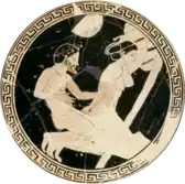 Interior of a Greek cup. The cup is black, with a white image of a woman on her knees and a man kneeing behind her; she is reaching behind her, grasping his penis.