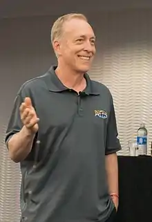 A smiling man wearing a grey polo shirt