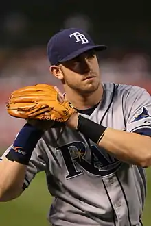 a right-handed fielding baseball player with his glove prepared to field a baseball while standing on the dirt of the basepath.