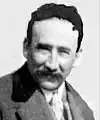 Black and white photo of a smiling man wearing a suit and a tie