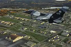 An F-16C Fighting Falcon from the 18th Aggressor Squadron is shown flying over Eielson AFB in 2009; the base's largest hangar, known as the "Thunderdome," is visible in the bottom left of the image.