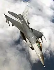 Upright aerial photo of gray jet aircraft flying above clouds