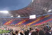 A full stadium, with fans holding up yellow, blue and red cards to make a giant mosaic.