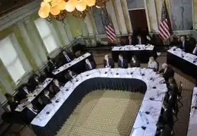 Eagle-eye view of a hearing room, with many seated members visible.