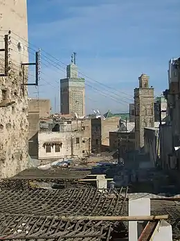 A picture of a sun-lit back alley with trash scattered across the area. Various buildings of varying architecture are clearly visible.