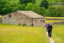 Tourists walking on a footpath, approaching a field barn in Muker