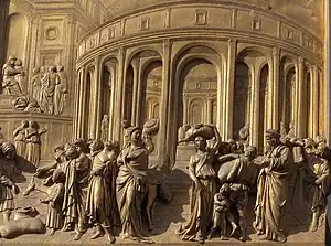 One of ten gilt bronze panels in low relief. It shows scenes in the story of Joseph visited in Egypt by his brothers, come to beg for grain in the famine. Rear left, Joseph sits on a throne while his brothers plead. Centrally is a large circular granary surrounded by arches. To the right, a group of people load a heavy sack onto a camel. To the left, a gold cup is discovered hidden in the sack of the youngest brother, a small child. The eldest brother tears his clothes in despair.