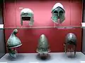 Ancient Greek helmets. Top line, from left to right: Illyrian type helmet, Corinthian helmet. Bottom line, from left to right: Phrygian type helmet, Pileus helmet with an olive branch ornament, Chalcidian helmet. Staatliche Antikensammlungen