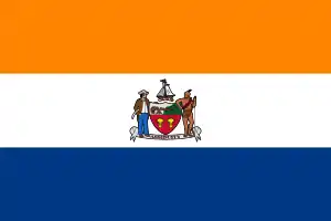 A flag with three equal horizontal stripes colored orange, white, and blue from top to bottom. In the center is the city seal (except for text and circular outline).